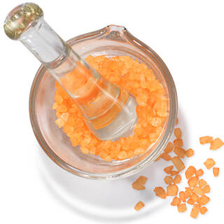 Mortier et pilon en verre avec des cristaux orange, representant de la vitamine C activee