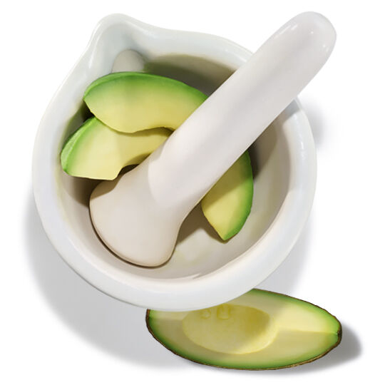 Mortier et pilon avec des morceaux d’avocat, illustrant l’utilisation de l’huile d'avocat comme ingredient nourrissant.