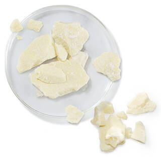 Coupelle en verre avec des morceaux de beurre de cacao, representant un ingredient hydratant.