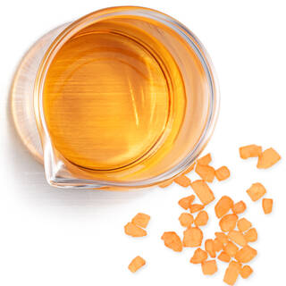 Becher de liquide dore avec des cristaux orange, illustrant la vitamine C