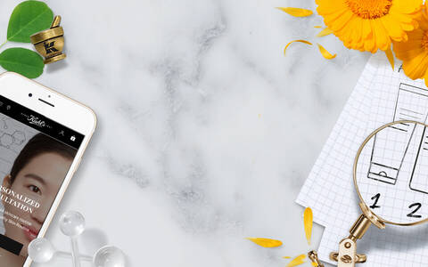 Image d'une consultation de soins de la peau personnalisee, affichee sur un smartphone, accompagnee de fleurs jaunes et d'un plan de formule sur un carnet.