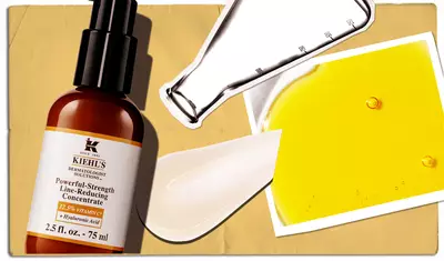 An arrangement of skincare products including a brown bottle of Kiehl's Powerful-Strength Line-Reducing Concentrate, a creamy white product, a petri dish with yellow liquid, and a sheet of paper with droplets, set against a textured beige background.