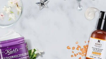 Creme de soin multicronique et serum anti-rides de Kiehl's poses sur un fond marbre, entoures de fleurs blanches et d'ingredients naturels.