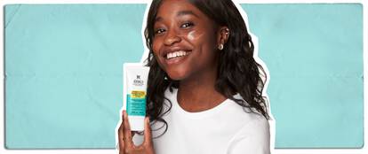 Une femme souriante tient un tube de lotion Kiehl's Expertly Clear et en applique une petite quantite sur sa joue.