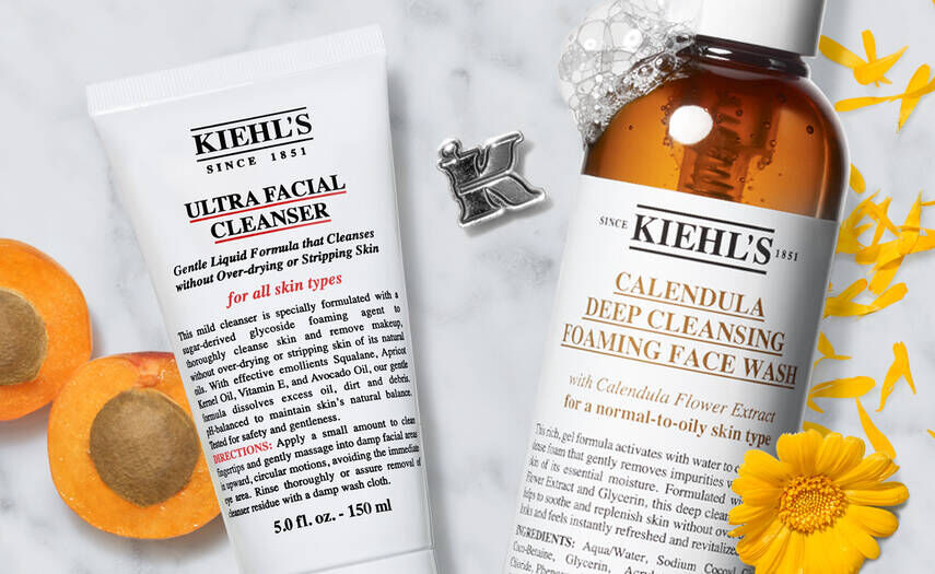 Une image presentant deux produits de soin de la peau de Kiehl's : un nettoyant facial ultra doux et un nettoyant moussant a la marigold, entoures de fleurs et d'abricots.
