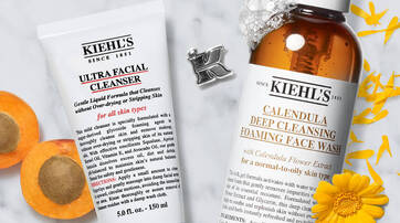 Une image presentant deux produits de soin de la peau de Kiehl's : un nettoyant facial ultra doux et un nettoyant moussant a la marigold, entoures de fleurs et d'abricots.