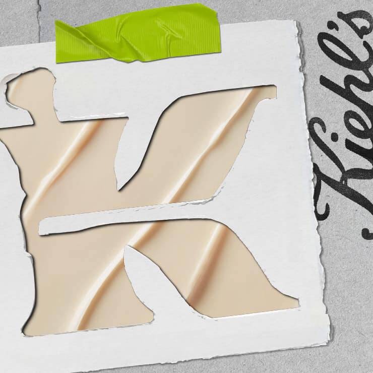 Grand « K » decoupe dans une feuille blanche, laissant apparaitre une texture creme en dessous, avec un morceau de ruban adhesif vert en haut.