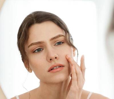Femme soignant son visage, examinant sa peau dans un miroir avec une expression attentive.