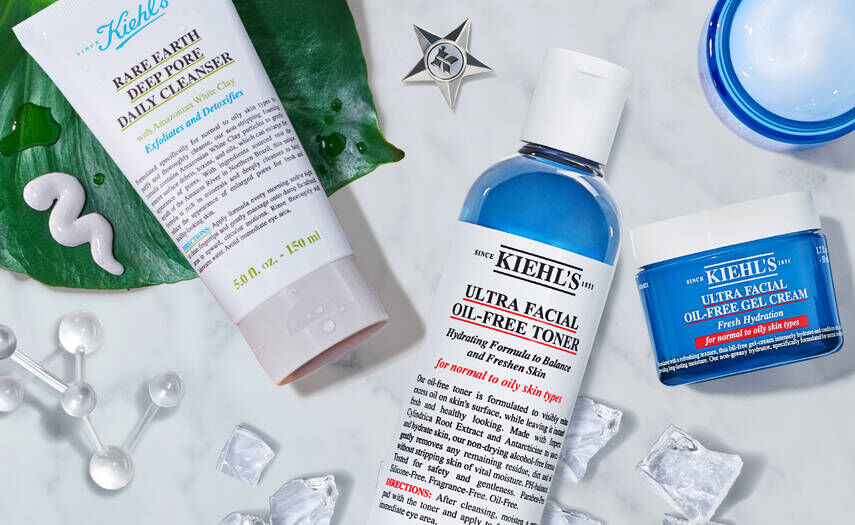 Produits de soin pour le visage de Kiehl's, incluant un nettoyant quotidien, un tonique et une creme hydratante, presentes sur une surface avec des elements naturels et des glacons.