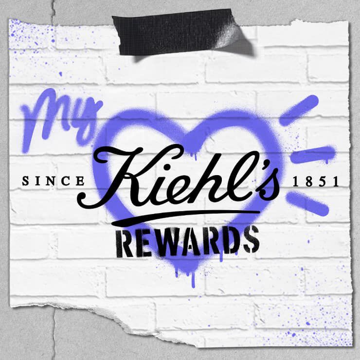 Affiche murale avec un coeur bleu peint en graffiti, le texte « My Kiehl’s Rewards » et la mention « Since 1851 » sur un fond de briques blanches.
