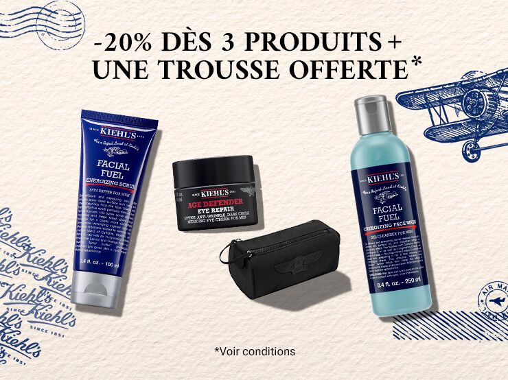 Produits homme Kiehl's (nettoyant, gommage Facial Fuel et soin yeux Age Defender) et trousse noire sur fond creme vintage aux motifs d'avion bleus.